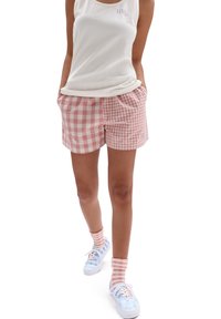 Vitt linne med logotyp, rosa rutig shorts och pastellblå sneakers med mönster. Strumporna är rosa och vita randiga.