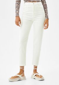 Vita högmidjade jeans med rak benvidd och synliga sömmar. I kombination med kraftiga plattformsandaler med korsade remmar.