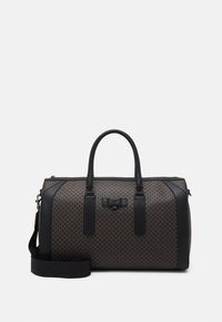 Sac de voyage à motifs marron avec des accents en cuir noir, deux poignées, une bandoulière réglable, fermeture éclair et un logo sur le devant.
