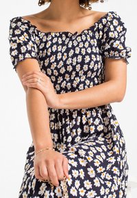 Námořnické šaty s bílým a žlutým květinovým vzorem, nařaseným živůtkem a krátkými nafouknutými rukávy. Mají splývavou sukni a texturovanou látku.