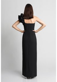 Czarna, dopasowana sukienka na jedno ramię z falbaniastym akcentem po lewej stronie. Gładki materiał z zapięciem na zamek z tyłu, suknia do długości podłogi.