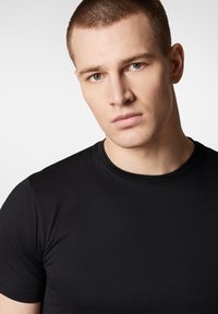 Czarna koszulka z okrągłym dekoltem wykonana z gładkiego, lekkiego materiału, z krótkimi rękawami, o dopasowanym kroju i minimalnej liczbie szwów.