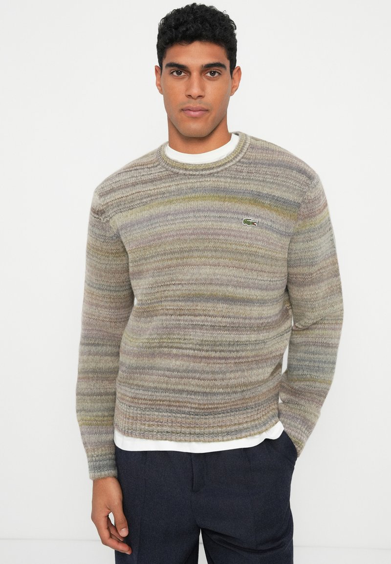 Multicolored knit sweater with a round neckline, featuring horizontal stripes in shades of gray, tan, and hints of yellow. Lacoste logo displayed.
