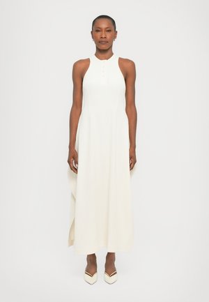 Vestido maxi sin mangas blanco con un cuello alto y cinco botones decorativos, con un corte holgado y una textura suave. Completado con unos zapatos planos de punta crema.