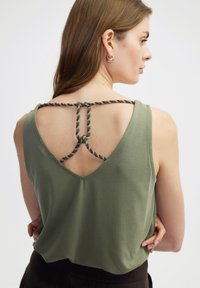 Olijfgroene mouwloze top met een V-vormige achterkant, voorzien van decoratieve gedraaide banden. Glad materiaal met een relaxte pasvorm en zonder patronen.