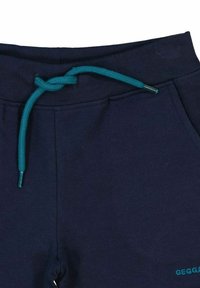 Mörkblå träningsbyxor med dragsko i midjan som har ett teal-färgat snöre och två sidofickor. Materialet verkar mjukt med en slät textur.