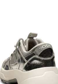 Metallisk silver sneaker med mesh- och texturerade detaljer, utrustad med en vit gummisula och en hälltab med "WODE"-logotyp.