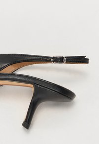 Sorte skinnhælte sandaler med åpen tå, ankelrem, sølvspenne og avsmalnet hæl. Glatt tekstur, minimalistisk design.