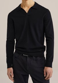 Svart långärmad polotröja i ett mjukt, texturerat stickat material med V-ringning och vikbar krage. Matchad med mörka denimbyxor.