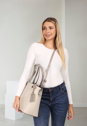 Beige leren handtas met dubbele handvatten en een afneembare riem. Soevele textuur, rechthoekige vorm en een aangehecht label met merkinformatie.