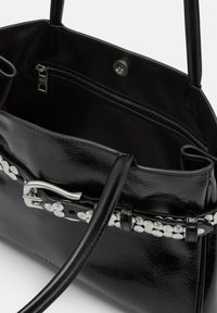 Czarna skórzana torebka o połyskującej powierzchni, z metalowymi elementami w kolorze srebra, dekoracyjnym akcentem w postaci klamry oraz wewnętrzną kieszenią na zamek.