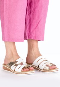 White slide sandals with multiple straps, featuring a metallic accent and cork sole. Textured detailing on the straps.