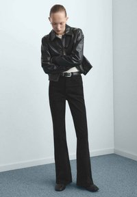 Czarna skórzana kurtka z prążkowanymi mankietami, biała koszulka i rozszerzane czarne dżinsy. Gładka tekstura, minimalistyczny design, w zestawie z czarnymi botkami na obcasie.