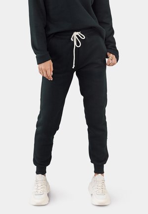 Schwarze Jogginghosen mit Kordelzugbund, elastischen Bündchen und einer glatten Textur, kombiniert mit weißen Turnschuhen.