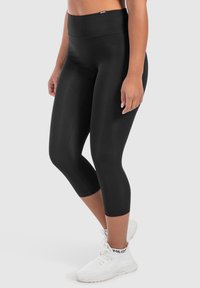 Leggings neri con vita alta, tessuto morbido e elasticizzato e design aderente. Indossati con scarpe da ginnastica bianche per creare contrasto.
