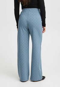 Blauwe wijdlopende broeken van zachte stof, met een stippenpatroon en een hoge taille. De achterkant benadrukt de uitlopende pijpen.