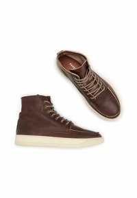 Bottes montantes en cuir marron avec semelle crème, présentant un bout arrondi, un lacet à l'avant et des accents brodés sur les côtés et la tige.