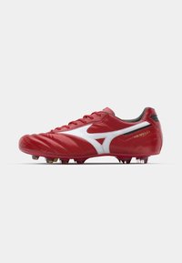 Crampon de football rouge avec un logo et des accents blancs, fabriqué en matériau synthétique lisse. Doté d'un bout arrondi et de plusieurs crampons sur la semelle.