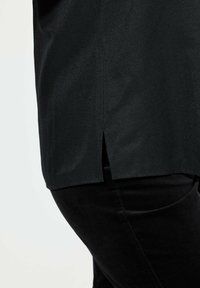 Zwarte top met een zijsplit, gemaakt van een gladde stof, gecombineerd met zwarte slim-fit broek, die een subtiele glans vertoont.