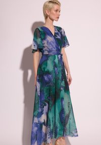 Sukienka maxi w przezroczystym materiale, z niebiesko-zielonym wzorem abstrakcyjnym, krótkimi falbaniastymi rękawami oraz wiązanym w pasie, tworzącym dopasowaną sylwetkę.