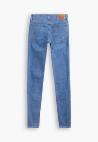 Jean skinny en denim bleu vu de dos avec deux poches, passants pour ceinture et un patch de marque en cuir marron sur la taille.