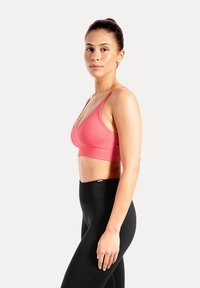 Sujetador deportivo rosa con escote en V profundo y tirantes anchos, combinado con leggings negros de talle alto que cuentan con una cintura texturizada.