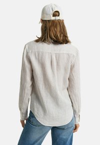 Gestreepte langarmshirt van lichtgewicht stof, met een button-down kraag, een rugplooival en een afgeronde zoom. Gecombineerd met lichtblauwe jeans.