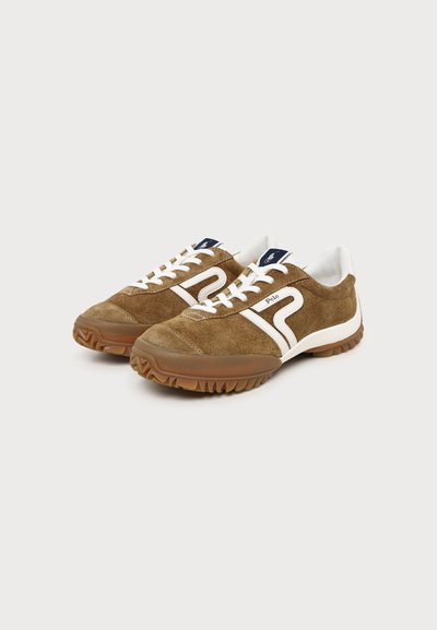 Paire de baskets en daim marron avec des lacets blancs, des semelles en gomme et un détail latéral blanc à rayures, posées sur un fond blanc uni.
