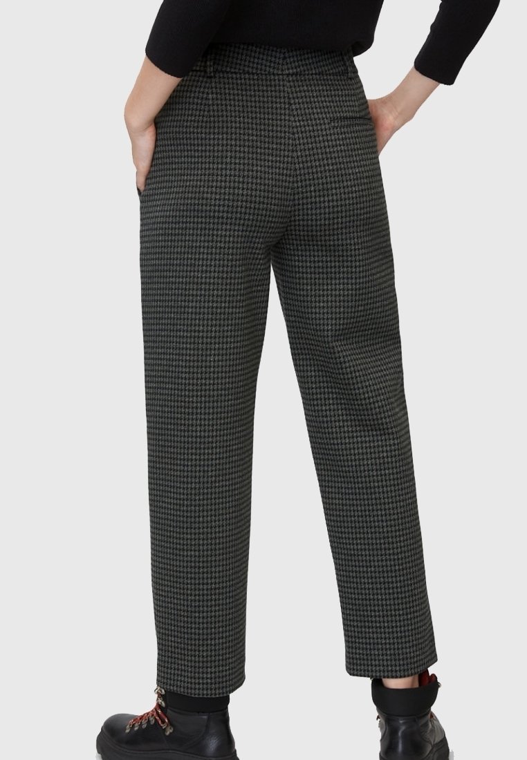 Personne portant un pantalon droit taille haute à motif pied-de-poule noir et gris, des bottes noires et un haut noir à manches longues.