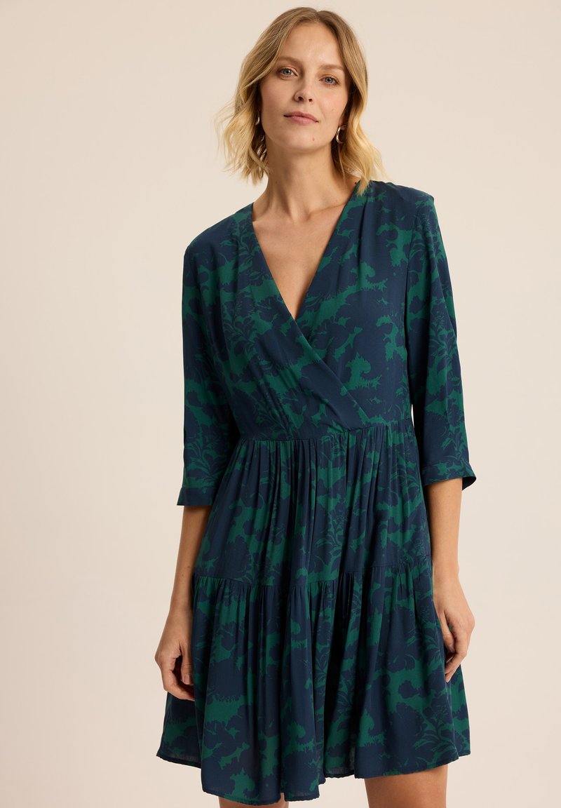 Granatowa sukienka z zielonym kwiatowym wzorem, lekki materiał, dekolt w serek, rękawy 3/4, rozkloszowany dół z marszczeniami, długość do kolan.