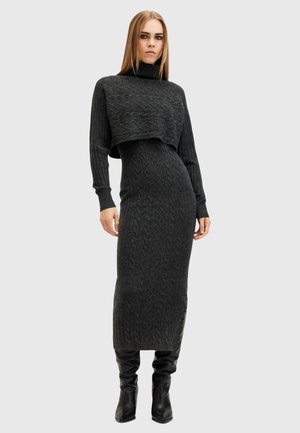 Grijze gebreide jurk met kabelpatroon, hoge halslijn en korte lijf. Aansluitend silhouet dat tot de knie reikt. Gekocht met zwarte kniehoge laarzen.