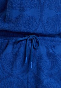 Plavi teksturirani pulover s detaljnim uzorkom, s vezanjem na struku i kontrastnim vrhovima vezica.