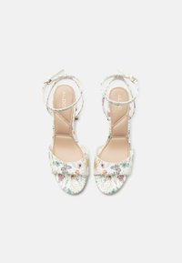 Sandalias blancas de punta abierta con estampado floral y de mariposas, tiras en el tobillo con hebillas y plantillas acolchadas beige con la marca ALDO.