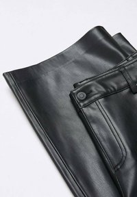 Pantalon en similicuir noir plié soigneusement, montrant la ceinture, la fermeture par bouton et les détails de couture des poches avant sur un fond blanc.