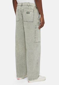 Volné svetle šedé denimové kalhoty s několika kapsami, fadovanou texturou a prošitým pasem. Na zadní kapse je umístěna nášivka s logem.