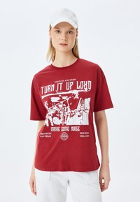 Camiseta de algodón roja con un diseño gr�áfico blanco que presenta texto e imágenes relacionadas con la música. Mangas cortas y cuello redondo.