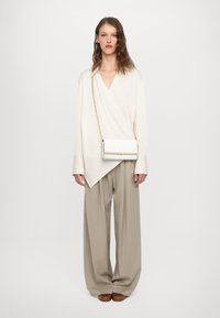 Blouse croisée blanche à manches longues, pantalon large beige, et un petit sac à main blanc avec des accents dorés sur une bandoulière chaîne.