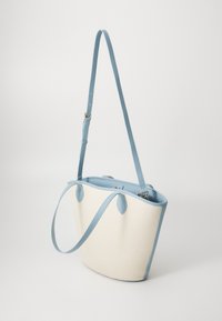 Kabelka s texturovaným krémovým exteriérem a světle modrými koženými akcenty, s jedním nastavitelným popruhem a zakřiveným siluetou.
