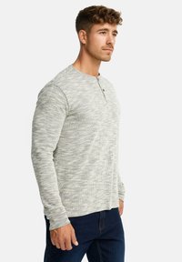 Langærmet, tekstureret grå skjorte med henley-udskæring og en knap. Brugt sammen med mørkeblå jeans.