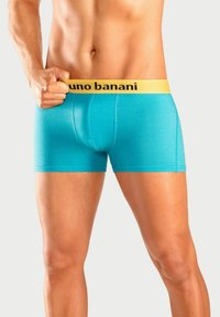 Turquoise boxer briefs with a yellow waistband featuring "bruno banani" in black text. The fabric is smooth, form-fitting, and stretchy.