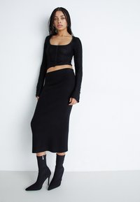 Svart langermet crop top med teksturert stoff, høyt liv svart skjørt, og tettsittende svarte ankelstøvler med spiss tær og glidelås.