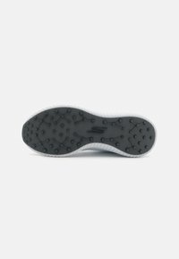 Sole of a shoe with a black rubber base featuring textured grip spots and raised circular patterns. White side detailing along the edges.