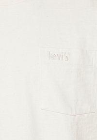T-shirt en coton blanc avec une poche frontale arborant un logo Levi's brodé. La texture est douce avec une coupe décontractée.
