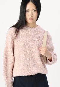 Pink, fluffy sweater made of soft material with a crew neckline and dropped shoulders. Model holds a light strap bag.