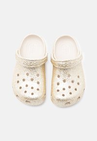 Ξύλινα παπούτσια με χρυσή γκλίτερ, κατασκευασμένα από ευλύγιστο υλικό, με οπές αερισμού και πίσω λουρί. Λεία εσωτερική υφή, ελαφρύς σχεδιασμός.