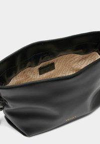 Sort læderhåndtaske med en glat tekstur, med en beige mønstret inderside og et lille logomærke indeni. Tasken har en trykknaplukning.