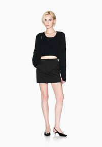 Maglione corto nero, minigonna nera e décolleté slingback nere. Il maglione ha una finitura testurizzata, dettagli minimi e una vestibilità ampia.