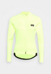 Pitkähihainen pyöräilypaita kirkkaan neonkeltaisena, jossa on etuvetoketju, mustat yksityiskohdat ja logopatchi vasemmassa yläkulmassa.