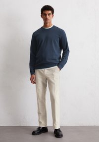Granatowy sweter z okrągłym dekoltem, w zestawie z kremowymi, dopasowanymi spodniami z bocznymi szwami oraz czarnymi, masywnymi butami.