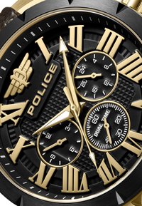 Svart och guld polisur med romerska siffror, texturerad svart urtavla och tre sub-dialer för dual tid och kronograffunktioner.